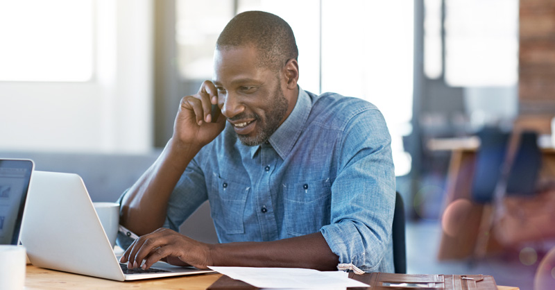 Smiling African American male on phone in front of laptop
