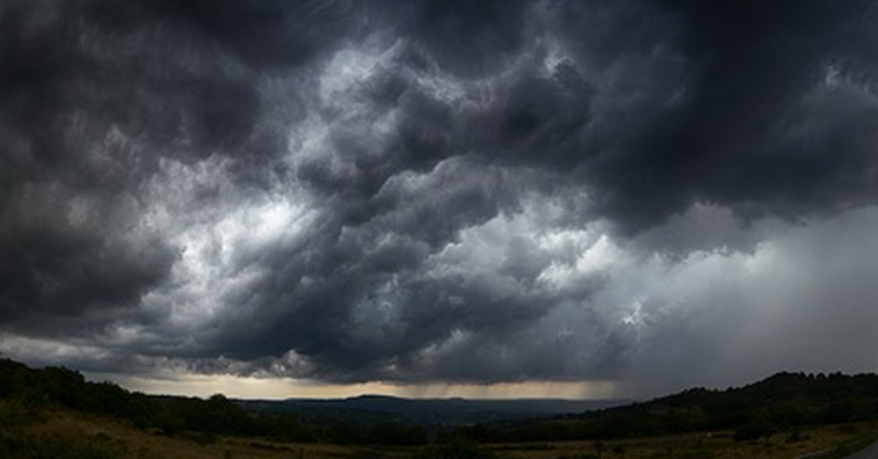 Dark storm clouds gathering over a rural landscape with rain visible in the distance.