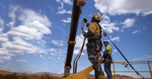 Workers wearing safety harnesses use a self‑retracting lifeline while working at height on a steel structure.