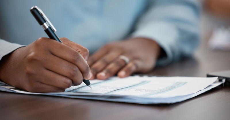 Close-up of a professional signing paperwork on a desk.