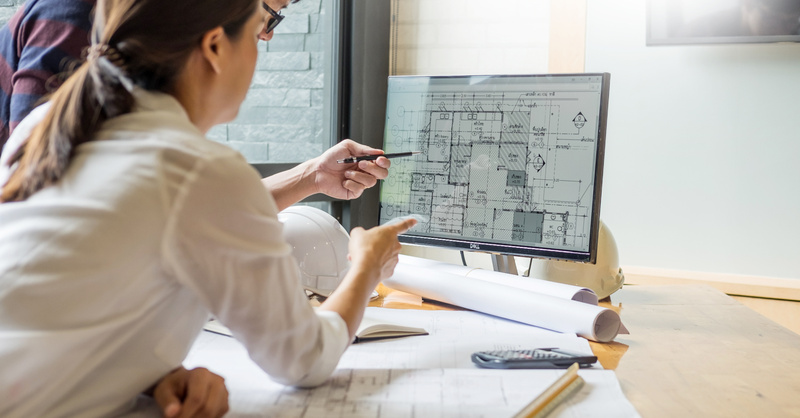 Two design professionals review architectural plans displayed on a computer monitor.
