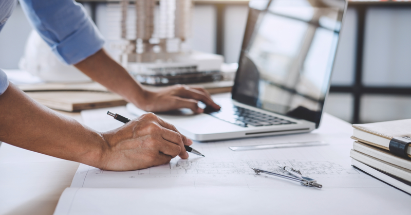 Professional reviewing plans and working on a laptop at a desk.
