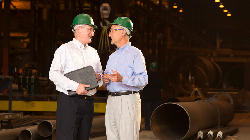 Two men wearing green hard hats in a warehouse