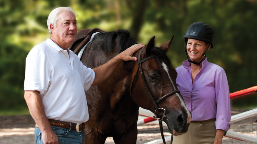 Senior man petting horse and woman standing next to horse