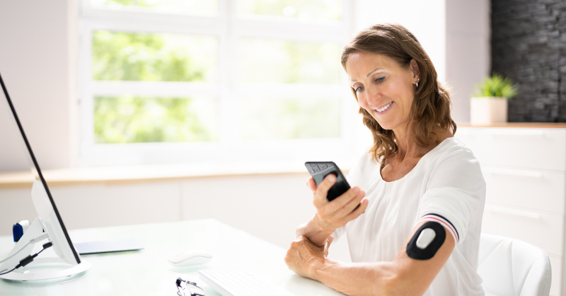 Person reviewing health information on a smartphone while wearing a remote monitoring device on the upper arm.