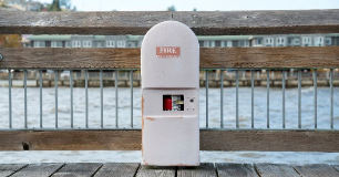 Fire extinguisher inside a labeled cabinet on a marina dock, with water and waterfront buildings in the background, representing marina fire safety, emergency preparedness, and fire prevention measures.