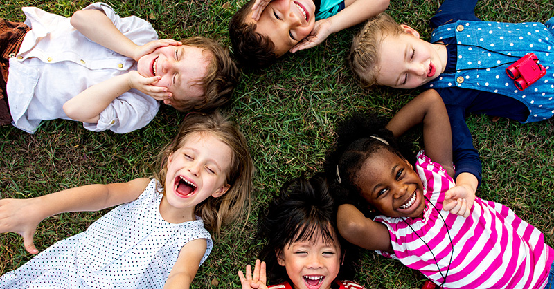Smiling children laying on the grass in a circle