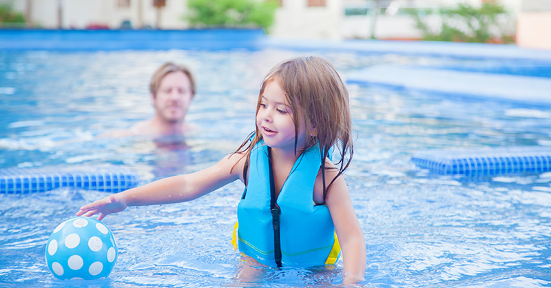 Child wearing a life jacket playing with a beach ball in a swimming pool