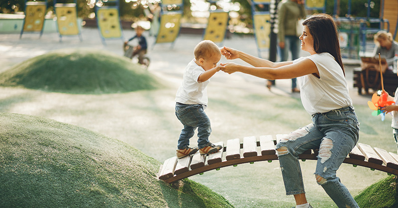Mother and son holding hands on a playground bridge obstacle
