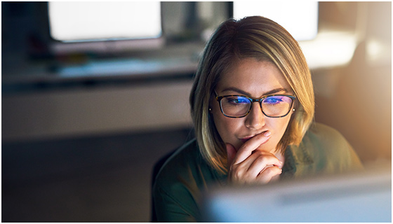 Woman with glasses thoughtfully staring at computer screen